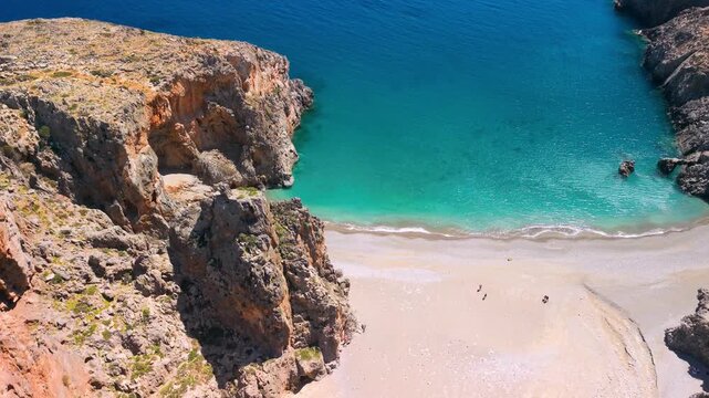 Aerial flight out of Agiofarango canyon over orange cliffs to turquoise sea and beach. Drone reveal of South Crete wild coast landscape with crystal clear water at sunny day. Scenic 4k stock video.