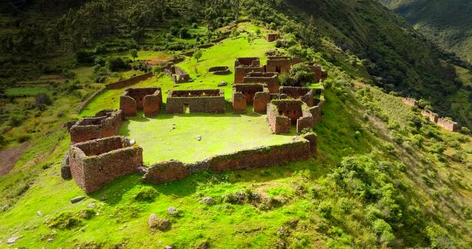 Ancient Inca archaeological site of Pumamarka, with stone ruins on green hillside in Sacred Valley, Peru. Aerial drone orbiting