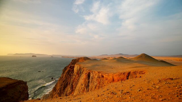 Handheld slow motion shot of a gentle wave rolling onto the shore at Paracas National Reserve, Peru. Cinematic coastal landscape with desert cliff under a warm golden sunset