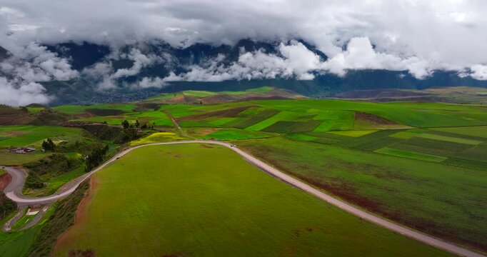 Vibrant green agricultural fields and rural road under dramatic clouds in Maras district of Sacred Valley, Peru. Aerial drone