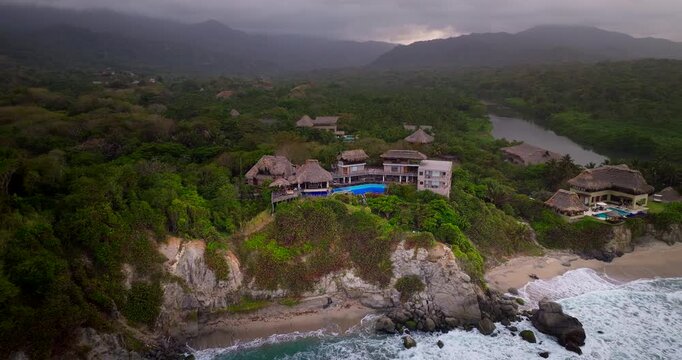 Luxury hotel with swimming pool on cliff overlooking beach and jungle near Tayrona Park, Colombia. Aerial drone orbiting