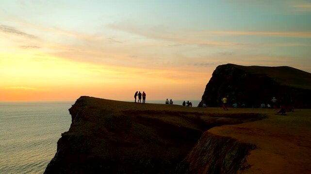 Silhouetted figures stand on a rugged cliff overlooking the ocean during golden hour at Paracas National Reserve, Peru