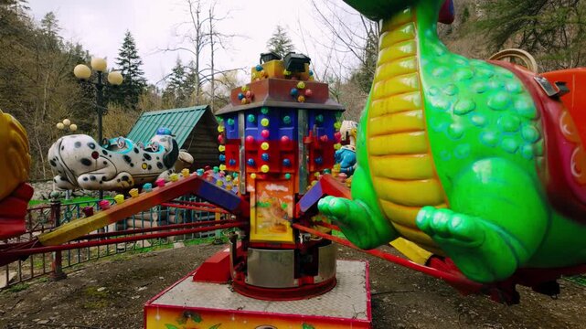 Detailed view of colorful carousel showing a green dragon and dalmatian dog themed seats around the illuminated central column in a quiet Borjomi amusement park.