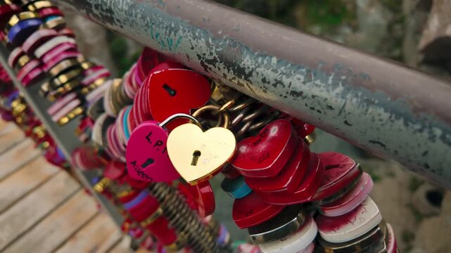 Close-up view of heart-shaped love locks, some with personalized inscriptions, fastened to a metal bridge railing in Tbilisi. Symbolizes romantic tradition for couples.
