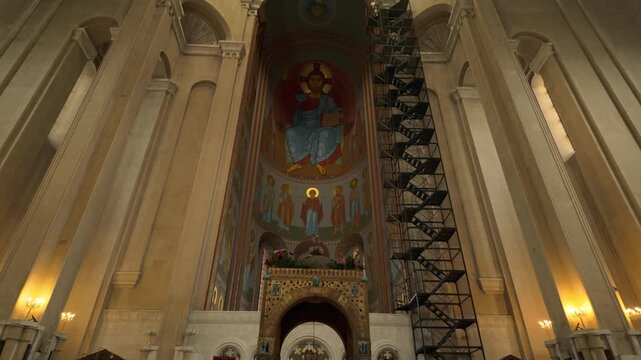 Impressive interior shot of the Holy Trinity Cathedral in Tbilisi, Georgia, focusing on a large religious fresco depicting Christ above the altar area, surrounded by the cathedral's grand architect...