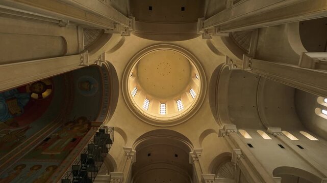 Majestic view looking upwards at the intricately designed dome and towering columns inside the Holy Trinity Cathedral in Tbilisi, Georgia. Natural light streams through upper windows, highlighting ...
