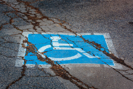 Wheelchair sign, a disabled parking spot, a blue and white sign on a cracked pavement