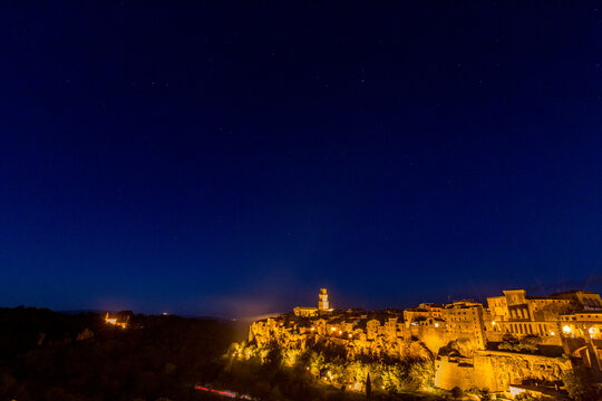 Starry sky. Nighttime view of city with clock tower and street light, Sovana, Tuscany, Italy, long exposure motion blur