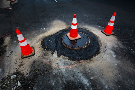 A flood of water from a sewer manhole cover and traffic cones on a road.