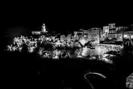 Black and white view of city at night with clock tower, Sovana, Tuscany, Italy, long exposure motion blur, car trails