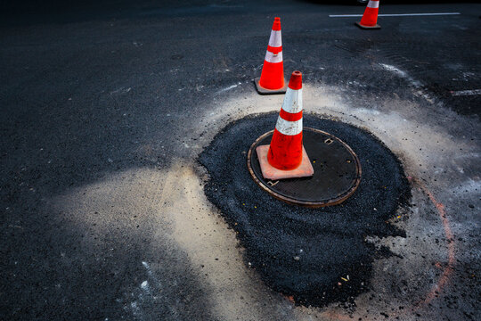 Road construction, flooding around a sewer manhole cover, traffic cones on the roadway.