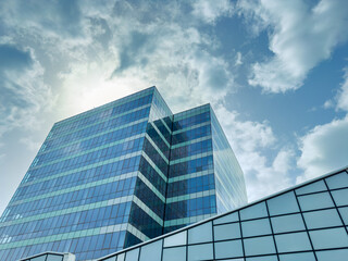 Fototapeta premium Sky above glass buildings in an urban area during the day with clouds and sun shining in the background
