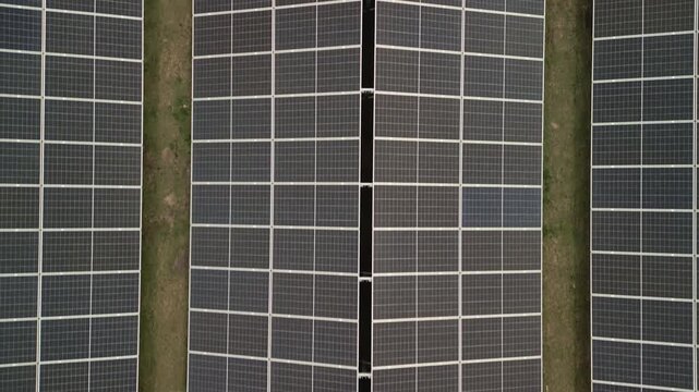 Aerial drone view of a photovoltaic solar panel array. Backward and upward movement gradually reveals the scale of the sustainable green energy farm.