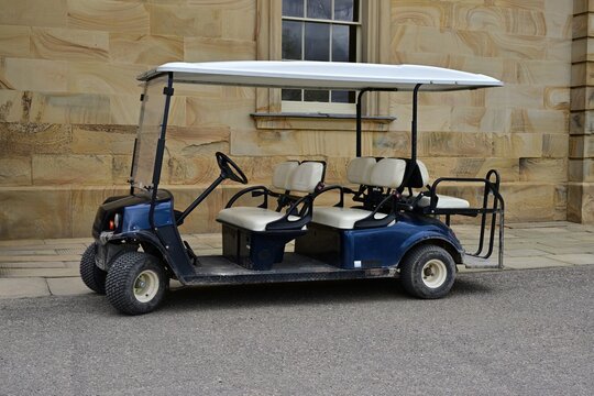 Blue and white electric golf cart parked beside stone wall