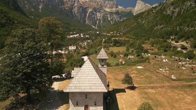 Aerial drone flyover of the iconic stone church in Theth village. Scenic mountain landscape of the Albanian Alps during a sunny summer day.