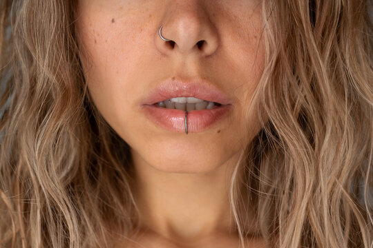 Close-up of young attractive blonde woman with fake nose and lip piercing, natural glossy lips and wavy hair. Edgy beauty style and self-expression concept