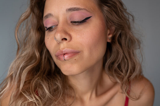 Portrait of young attractive blonde woman with fake nose and lip piercings, pink eye makeup and winged eyeliner. Beauty, self-expression and edgy feminine style concept