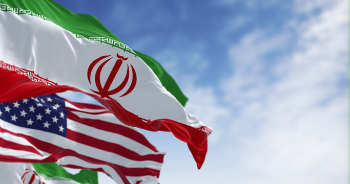 The national flags of Iran and the USA waving on a clear day