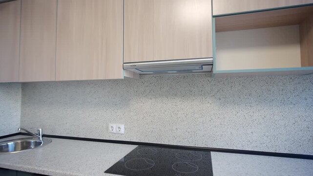 Kitchen displays light wooden upper cabinets and deep teal lower drawers. Speckled grey backsplash complements sleek induction cooktop