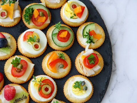 Flat lay overhead of colorful appetizers on dark stone serving dish placed on a marble counter for a party gathering. 