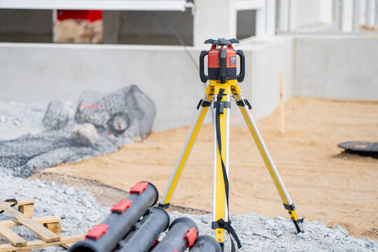 High-tech laser leveling instrument on a tripod stand used by engineers for site preparation and alignment of infrastructure elements at an outdoor construction project