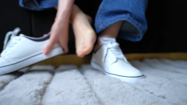 Woman enters frame in white shoes, sits down, removes loafers and scratches both itchy feet. Concept of skin irritation, discomfort, foot care, hygiene or possible dermatology issue. 