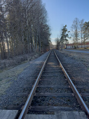 Obraz premium Railway tracks leading through rural landscape and forest under clear blue sky