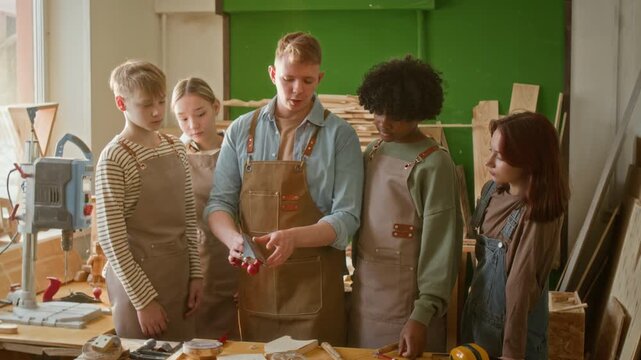 Gen Z woodworking instructor telling group of teenagers how to use hand plane properly while they attending carpentry masterclass