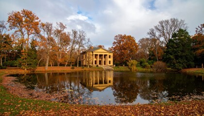Fototapeta premium Historic Neoclassical Mansion Reflected in Autumn Lake Surrounded by Vibrant Fall Foliage.