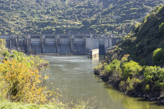 View of the Douro River dam with its massive concrete spillways and infrastructure surrounded by lush green hills and terraced slopes in Portugal.