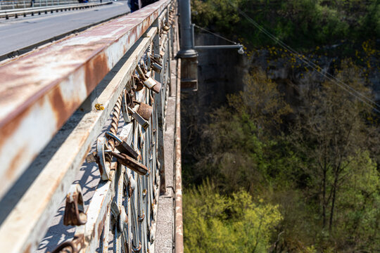 View of love locks attached to a rusty metal bridge railing overlooking a deep canyon with lush green trees in Kamianets'-podil's'kyi, Khmel'nyts'ka oblast, Ukraine.