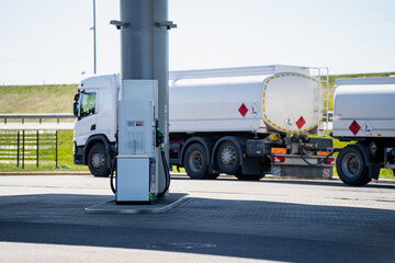 Naklejka premium White fuel tanker truck parked at a modern gas station pump for refueling and logistics distribution of flammable liquids during a sunny day in an industrial transport zone