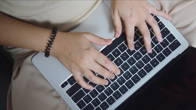 Person's hands using a silver laptop keyboard, working or studying online in a comfortable setting, demonstrating productivity and connectivity in the digital age