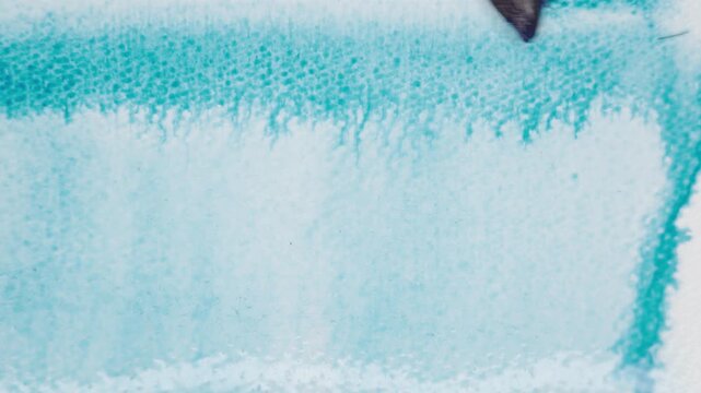 Close up of blue watercolour drawing paints on paper. Artist draws with a brush, liquid analog effects for background with copy space for text in center. 
