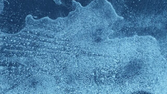 Extreme macro close-up of cracked blue melting ice texture in time lapse. Abstract frozen water surface with translucent crystal patterns, condensation and thawing details in studio lighting.