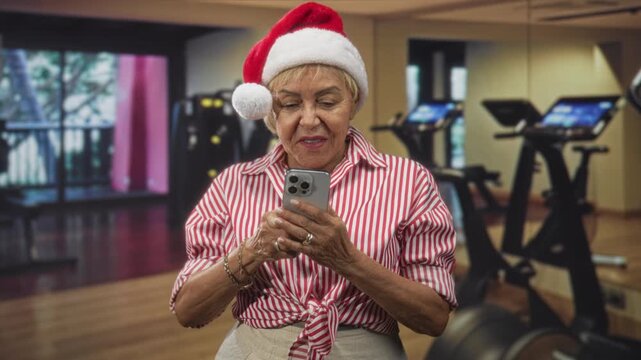 Woman holds smartphone and types with hands in studio wearing santa hat and striped blouse; cheerful holiday call.