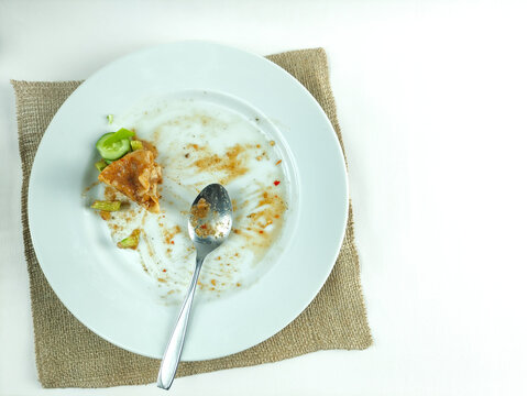 Dirty plate with leftover siomay and spoon on burlap background top view
