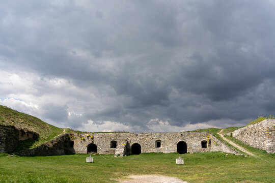 View of Kamianets-Podilskyi Castle stone walls with arched openings under a dramatic stormy sky and green grassy slopes Kamianets-Podilskyi, Khmelnytska oblast, Ukraine.