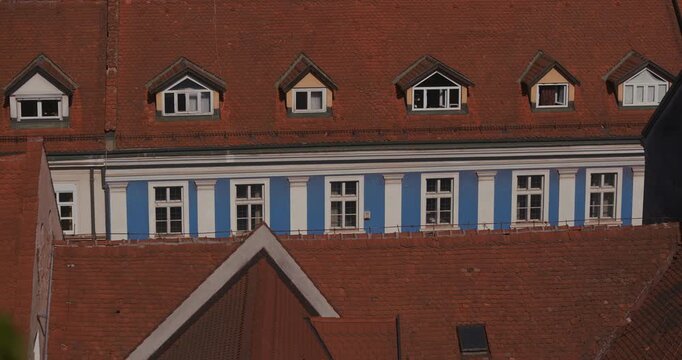 Elevated view of a historic building with red tiled roof, dormer windows, and blue facade details in Zagreb, Croatia.