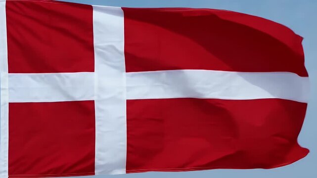 The video captures the Danish flag, known as the Dannebrog, gently waving in the breeze against a clear blue sky.