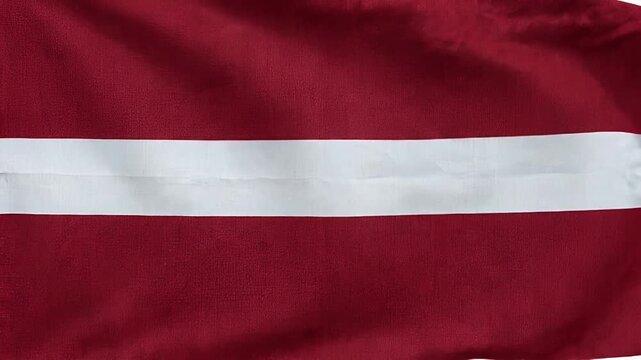 A close-up shot of the national flag of Latvia waving gently in the wind. The flag features horizontal stripes of carmine red, white, and carmine red.