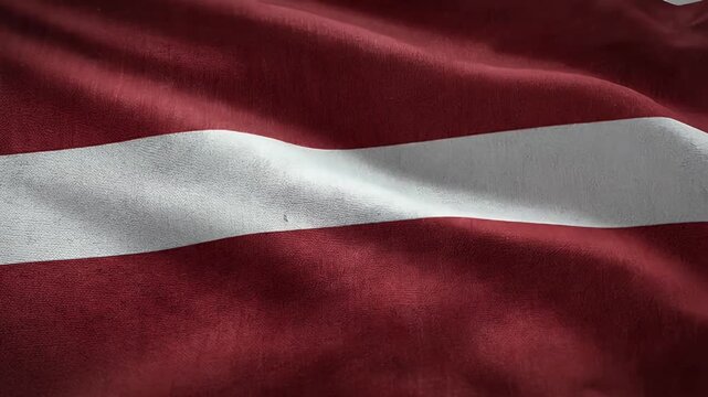 A detailed close-up of the Latvian flag, showcasing its distinctive red and white colors. The fabric appears textured and is gently rippling, highlighting the flag's classic horizontal-striped design.