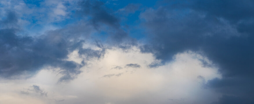 Dramatic panoramic sky with dark blue clouds and bright clearing in the center, contrasting cloudscape at dusk