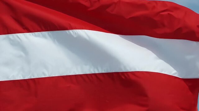 A close-up shot of the Austrian flag waving in the wind against a blue sky. The flag consists of three equal horizontal bands of red, white, and red.