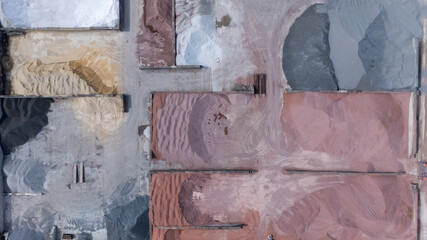 Top down aerial view of different piles of sand, gravel and raw construction materials stored in an industrial yard. Abstract patterns, textures and colors created by mineral aggregates from above. © MSG919