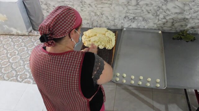 A Latina chef is making achira cakes with flour and then placing them on a metal tray on a table in a kitchen in Yaguara, Huila, Colombia. Concept of small business and raw food
