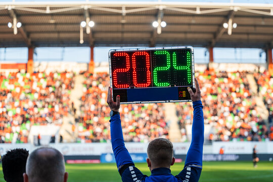 Rear view of a fourth official holding an electronic substitution board showing numbers 20 and 24 at a football stadium.
