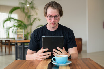 Authentic portrait of a Scandinavian man using a digital tablet while sitting in a cafe with glasses. © Ranta Images