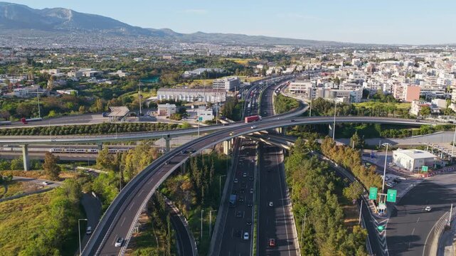 Aerial footage showing a complex multi-level highway interchange with cars and trucks driving, revealing the urban sprawl of a modern city with mountains in the background during a sunny day