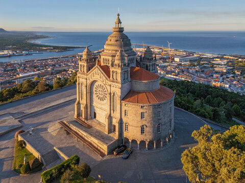 Aerial close view of Santa Luzia sanctuary in Viana do Castelo at sunrise, highlighting the ornate basilica facade, port district, and Atlantic shoreline in warm early light.